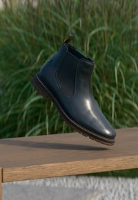 Fekete bőr Chelsea boot elegáns dizájnnal, kerek orral, rugalmas oldalsó panelekkel és texturált gumitalppal, fa felületen bemutatva.