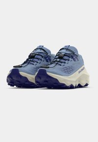 Ανοιχτό μπλε παπούτσια για τρέξιμο σε μονοπάτια με υφή στ ο πάνω μέρος, μοβ λεπτομέρειες και χοντρή λευκή σόλα με έντονα πέλματα για καλύτερη πρόσφυση.