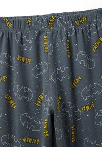 Pantalones cortos de pijama grises y suaves con un diseño repetido del logo de Batman y el texto amarillo "BATMAN" con manchas blancas que parecen estrellas. Cintura elástica.