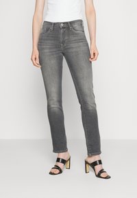 Tajta grå denimjeans med midjehög midja, fem fickor och subtila slitningar, tillsammans med svarta högklackade sandaler.