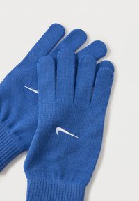 Gants en tricot bleus avec un poignet côtelé. Comprend le logo Nike blanc. Les gants ont cinq doigts et un tissu texturé pour une meilleure prise.