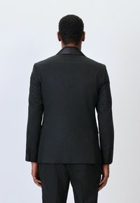 Mustmustri tekstuuriga must ülikonna jakk, millel on teemantmuster, satiinist krae ja nööpidega mansetid. Kohandatud lõige, et saavutada kaasaegne siluett.