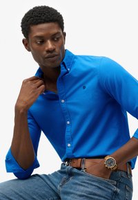 Blauwe button-up shirt gemaakt van katoen, met een klassieke kraag en opgerolde mouwen, gecombineerd met denim jeans en een leren bruine riem.