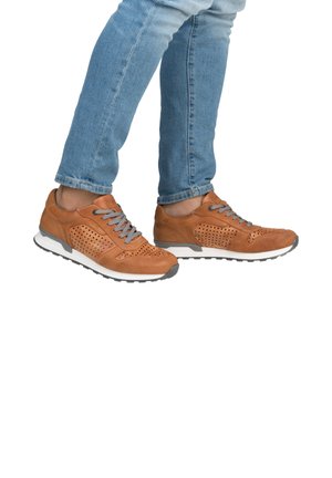 Baskets en cuir marron avec un design perforé, lacets gris, semelle blanche et accents gris. Portées avec un jean bleu clair.