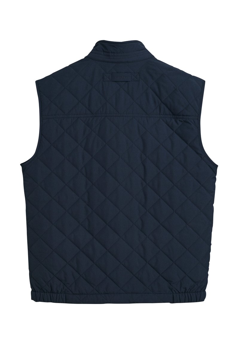 Chaleco acolchado azul marino con cuello alto, dobladillo elástico y sin mangas. Presenta una textura suave y un logo sutil en relieve en la parte trasera.
