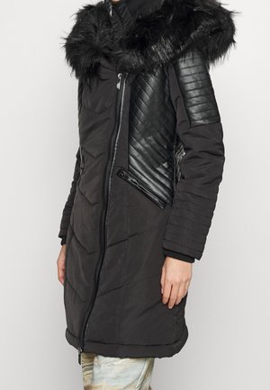 Abrigo acolchado negro con textura acolchada, capucha de pelo sintético y acentos de cuero en las mangas. Bolsillos con cremallera y puños de canalé.