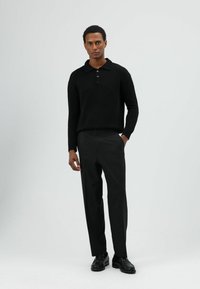 Zwart gebreide polotrui met kraag en drie knopen, gecombineerd met op maat gemaakte zwarte broek en zwarte leren schoenen. Minimalistisch design.