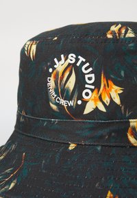 Mustahattu mustasta denimkankaasta, jossa on kukkakuosi. Hatussa on valkoinen logo, jossa lukee "JJ STUDIO DENIM CREW" ja erottuva vyö.