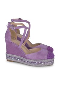Sandales compensées en daim violet avec un capuchon de orteil tressé violet et une semelle ornée de strass. Deux brides de cheville avec des boucles en métal.