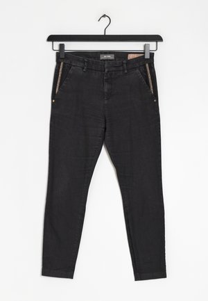 Czarne, dopasowane spodnie z gumką w talii i szlufkami, przednimi kieszeniami ozdobionymi brokatową lamówką, wiszące na czarnym wieszaku na białym tle.