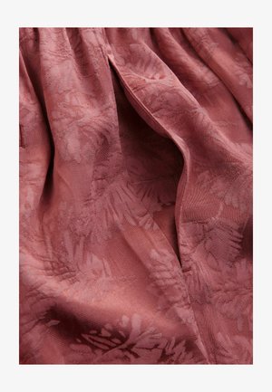 Tissu rose avec un motif floral texturé. Design drapé avec un doux éclat, présentant des variations subtiles de couleur et de lumière.