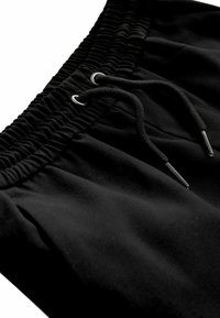 Zwarte shorts van zacht materiaal, voorzien van een elastische tailleband met geplooide textuur en een trekkoord met zwarte metalen uiteinden.