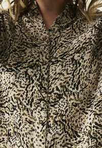 Košilová košile s vířícím leopardím vzorem v hnědé, zelené a béžové barvě, vyrobená z texturované tkaniny s klasickým límečkem a hnědými knoflíky.