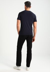 T-shirt aderente blu navy in cotone, abbinata a jeans neri; modello di spalle, sneakers bianche, design semplice senza decorazioni.