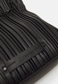 Black pleated leather bag with a smooth finish and embossed "KARL LAGERFELD" logo; features a chain accent and a flat base.