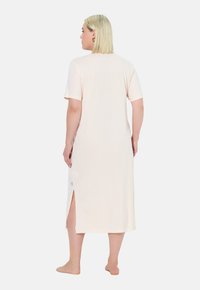 Camicia da notte a maniche corte, lunghezza al ginocchio, in morbido tessuto rosa con aperture laterali e minimalismo nei dettagli. Taglio semplice, vestibilità casual.