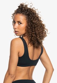 Reggiseno sportivo nero a coste con schiena larga e spalline. Texture liscia, design aderente e accento con logo sulla fascia.