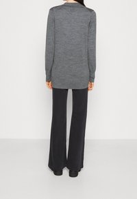 Szary sweter z długim rękawem i okrągłym dekoltem, w zestawie z czarnymi spodniami w kształcie dzwonów. Materiał wydaje się miękki i fakturowany.
