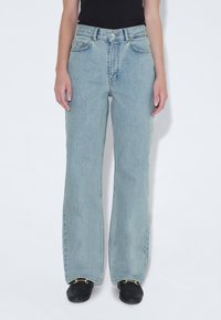 Jeans de color azul claro con un corte relajado, cintura alta y piernas anchas, confeccionados en denim. Cuenta con cinco bolsillos y un cierre de botón.