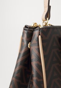 Sac à main marron à motifs avec un matériau synthétique texturé, des ornements dor�és et des accents beige clair. Il est équipé d'une poignée supérieure et d'une fermeture éclair.