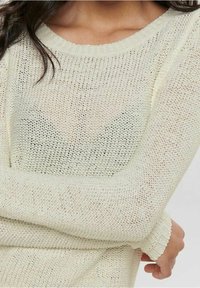 Cremefarbener Strickpullover mit einem lockeren, strukturierten Muster und rundem Halsausschnitt. Lange Ärmel mit enganliegenden Bündchen.