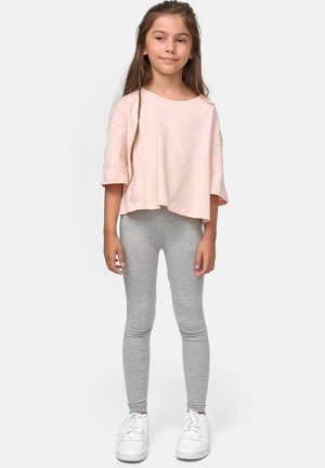 Kortermet, cropped lys rosa t-skjorte kombinert med grå leggings og hvite joggesko. Stoffet ser mykt ut og har en uformell design.
