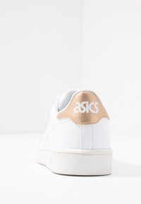 Weißer Sneaker mit einem strukturierten Lederhekelelement in Gold. Verfügt über eine glatte, schnürbare Vorderseite und eine Gummisohle. ASICS-Logo an der Ferse.