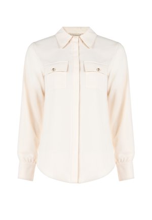 Blusa color crema realizzata in tessuto morbido, con colletto classico, maniche lunghe, due tasche sul petto con dettagli in bottone e orlo arrotondato.