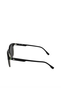 Czarne okulary przeciwsłoneczne o kwadratowym kształcie, z szarymi soczewkami i zielonymi akcentami na zausznikach. Na zauszniku znajduje się małe logo.