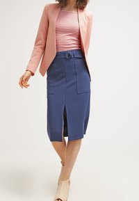 Námořnická tužková sukně s předním rozparkem a dvěma náprsními kapsami, doplněná růžovým blejzrem a pruhovanou blůzou. Měkká textura látky.