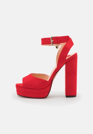 Sandales à plateforme en suède rouge avec un bout ouvert, un large talon carré, une bride de cheville avec une boucle en or et un charm en forme de cœur.