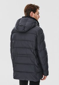 Padded jacket in dark gray, featuring a hood, horizontal quilted pattern, and fleece lining at the collar. Smooth, water-resistant material.