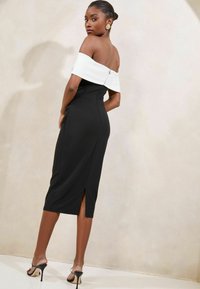 Čierne midi šaty s bielymi rukávmi bez ramienok. Majú priliehavý strih, bočný rozparek a zapínanie na zips na zadnej strane. Hladká textúra látky.
