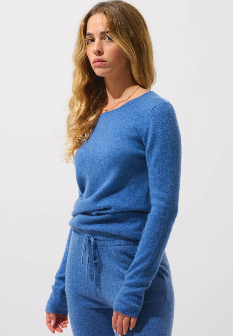 Blå stickad tröja med långa ärmar och rund halsringning, ihop med matchande byxor med dragsnörning. Mjuk textur och avslappnad passform.