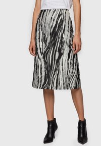 Femme portant une jupe midi à imprimé abstrait noir et blanc, un top blanc rentré et des bottines noires à bouts pointus.
