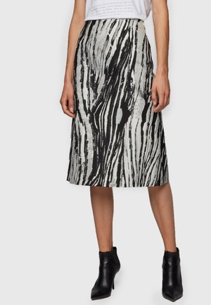 Mujer vestida con una falda midi de estampado abstracto en blanco y negro, una blusa blanca metida por dentro y botas de tobillo negras con punta afilada.