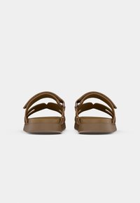 Braune Sandalen mit offenem Design und mehreren Riemen, ausgestattet mit einer flachen, breiten Sohle mit glatter Textur und einfachen Hardware-Accents.