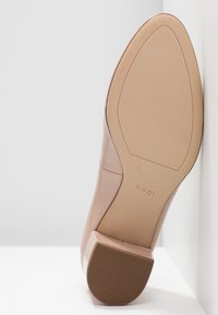 Beige lackläderhögklackad sko med fyrkantig tå, strukturerad gummisula och en blank yta. Har en diskret logotyp nära hälen.