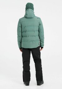Grüne gepolsterte Jacke mit Kapuze, schwarze Hose und gestrickte Mütze, mit glatter Textur und taillierter Passform, aus der Rückansicht.