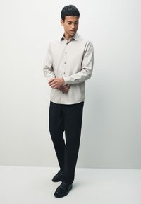 Light beige button-up shirt with a textured pattern, long sleeves, and standard collar, paired with black trousers and black shoes.