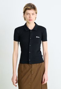 Polo preto de manga curta com frente de botão, colarinho clássico e detalhe do logótipo branco no peito, feito de tecido de algodão suave.