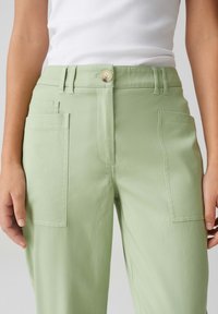 Pantalons cargo vert clair en tissu doux, avec des poches avant, une fermeture à boutons et une coupe droite.