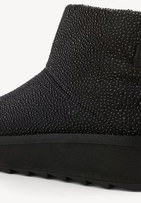 Schwarzer Knöchelboot mit strukturiertem Obermaterial, das mit kleinen glänzenden Nieten bedeckt ist, und dicker Sohle mit gerilltem Profil für besseren Halt.