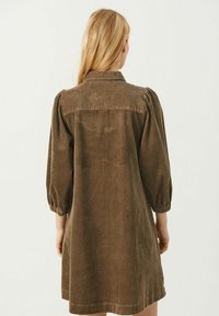 Brun velourklänning med krage, puffärmar och texturerad ribbad mönster. Längden på kjolen är ovanför knäet.