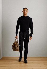 Black long-sleeve sweater and black joggers, carrying a brown bag. Black sneakers complete the outfit. Simple, modern design, minimalist style.