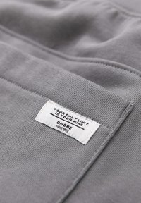 Zbliżenie na szarą tkaninę z białą prostokątną metką z napisem "Twoją jedyną granicą jest twój umysł" oraz marką "OMBRE od 1985".