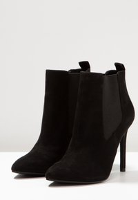 Černé semišové kotníkové boty s špičatou špičkou, elastickými bočními panely a stiletto podpatky; hladká textura a minimalistický design.