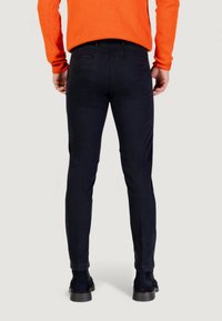 Pantalons en velours côtelé noirs à coupe slim. Ils présentent des poches arrière et une texture lisse, associés à un pull orange et des chaussures foncées.