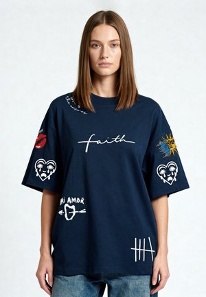 Vrouw draagt een navy oversized T-shirt met ontwerpen waaronder "faith", witte harten, "mi amor", een zon en een maan en telstrepen.