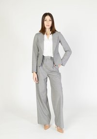Completo a quadri grigio con giacca su misura e pantaloni a gamba larga, abbinato a una camicia bianca con sottili accenti rosa e blu.